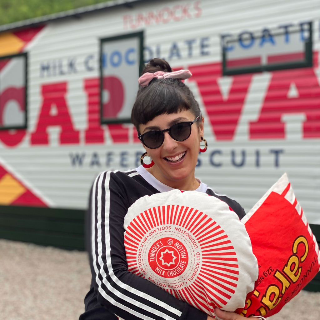 Nikki McWilliams holding Tunnocks Teacake cushions in front of the Tunnocks Caramel Wafer Caravan.